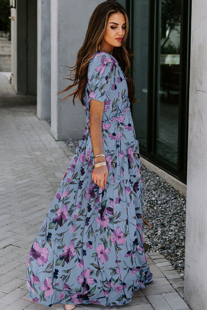 Vestido largo azul cielo con estampado floral intenso, cuello de pico y volantes, y manga corta
