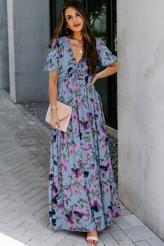 Vestido largo azul cielo con estampado floral intenso, cuello de pico y volantes, y manga corta