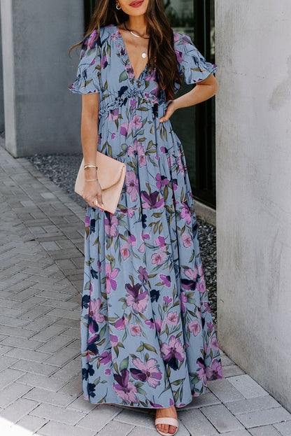 Vestido largo azul cielo con estampado floral intenso, cuello de pico y volantes, y manga corta
