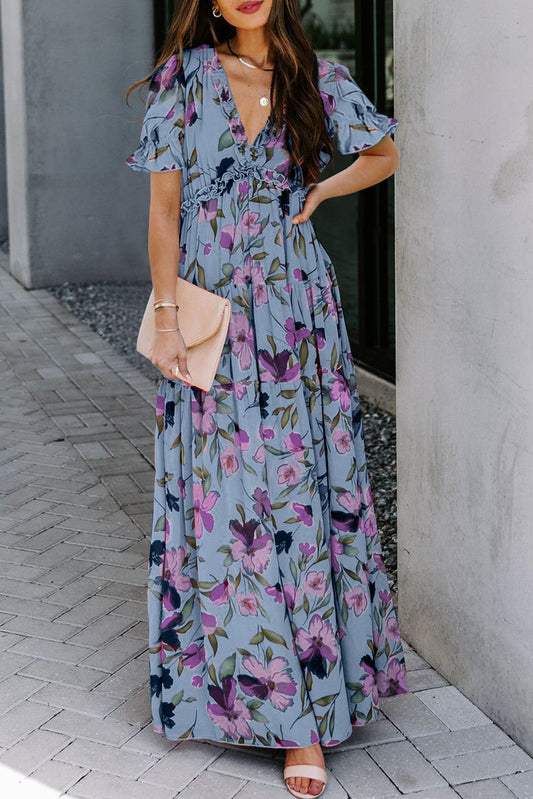 Vestido largo azul cielo con estampado floral intenso, cuello de pico y volantes, y manga corta