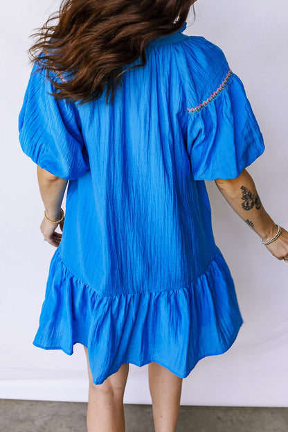 Vestido con bordado de flores azules, cuello dividido, mangas cortas abullonadas y dobladillo con volantes